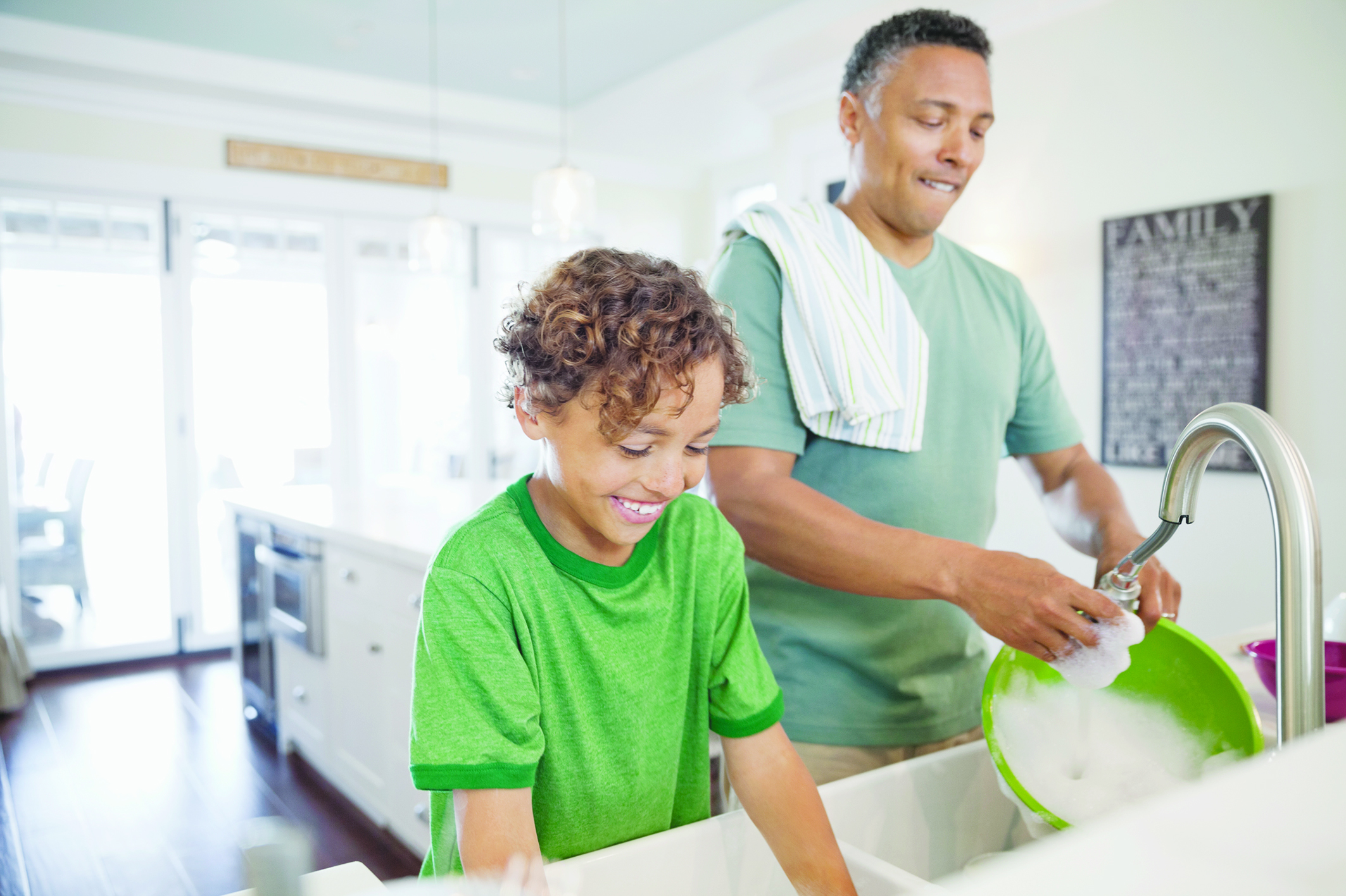 Mature father and son washing dishes together at kitchen sink
