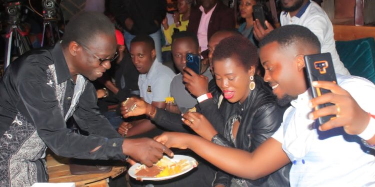 Moses Matovu serves cake to his fans. Photo by Joseph Kasigwa.