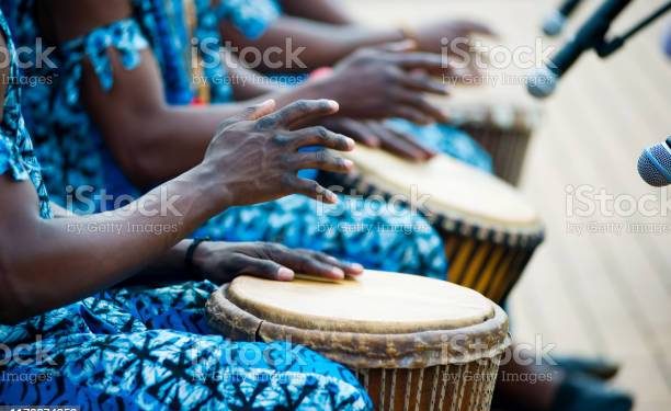 hands of African drummers in blue costumes and traditional drums in front of microphones at a performance